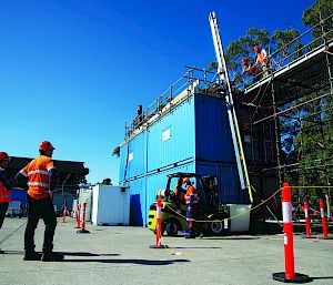 A group wearing hi-vis and hard hats look at a drill that is several metres long. There are blue shipping containers in the background.