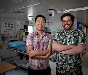 2 people stand in a medical room, smiling to the camera.