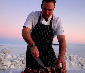 Chef slicing up scotch fillet with sunset over fast ice