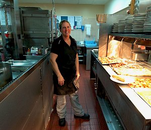 The station chef stands in the kitchen, near the bain marie full of freshly-cooked food.