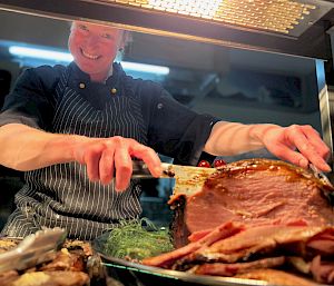Chef carving a ham leg smiling at camera