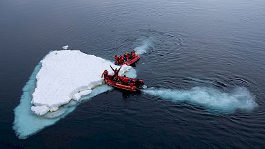 2 small boats push a floating piece of ice through the water.