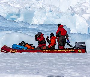 3 expeditioners in a small, red boat motor through icy water.