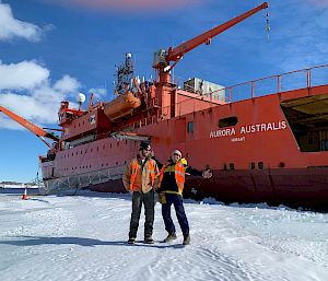 Two expeditioners standing in front of ship parked in ice