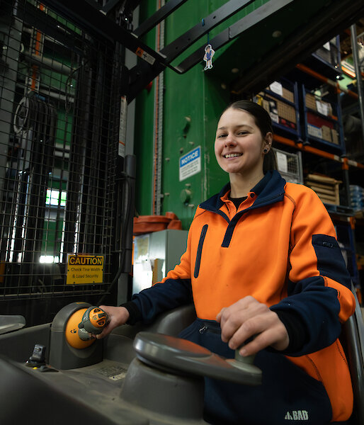 A woman in hi vis orange on a forklift