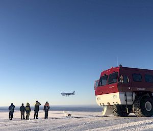 A group of people standing next to a bus, watching a plane land on the ice.