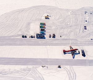 An aerial photo of an ice runway with a small aircraft and a row of parked vehicles.