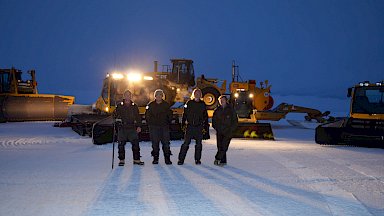 Expeditioners standing in the lights of plant equipment on runway at twlight