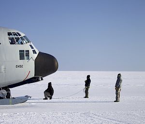 Three people stand in front of the nose of a large aircraft on the ice.