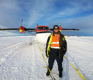 Man posing on the ice in front of red and white twin engine aircraft
