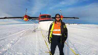 Man posing on the ice in front of red and white twin engine aircraft