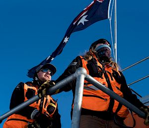 Low angle of expeditioners wearing high vis, on deck of building with Australian flag behind