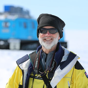 Man in sunglasses with blue over-snow vehicle in background.