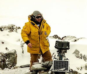 Person in yellow coat beside camera and solar panel.