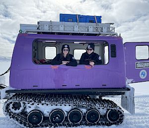 2 expeditioners lean out the window of a purple vehicle.