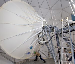 A large white satellite dish is pushed by an expeditioner inside a geodesic dome structure.