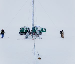 Expeditioners at the base of an antenna mast in front of a green tracked vehicle.