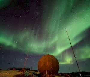 Green lights in night sky over tall radio masts and a dome structure.