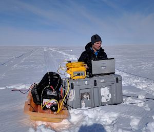 Expeditioner kneels with equipment on the ice.