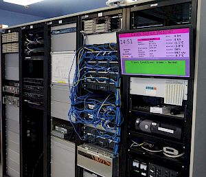 Rack of servers, computer equipment and a screen showing live data of Casey station's weather.