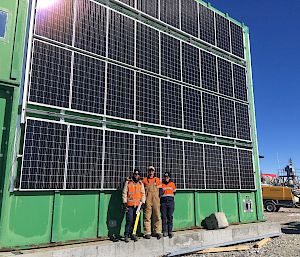 Three tradespersons standing in front of solar panels attached to building