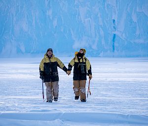 2 expeditioners walk across the sea ice holding hands.