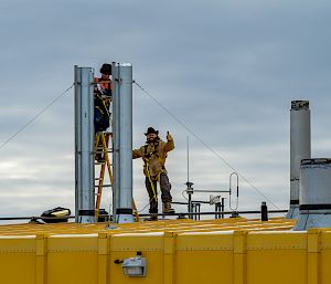 2 expeditioners work on the roof of a yellow building.