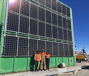 Three tradespersons standing in front of solar panels attached to green building.