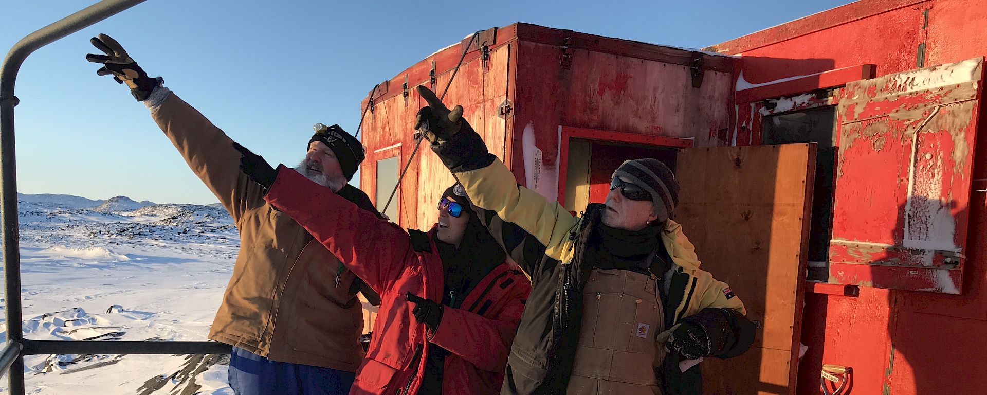 Three tradespeople stand outside a red field hut.