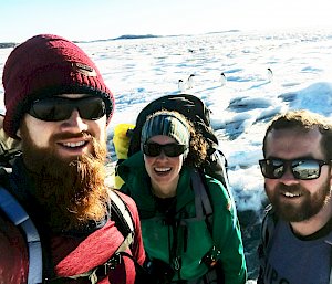 Three people in sunglasses with snowy background.