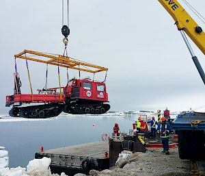 Crane lifting over-snow vehicle off barge at wharf.