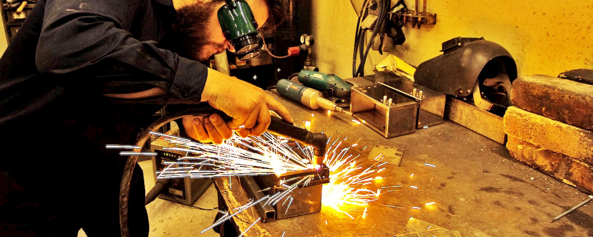 Person welding at a workshop bench wearing goggles.