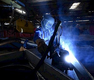 Person welding with mask on bathed in blue light from flame.