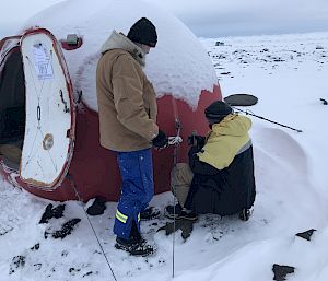 Two expeditioners undertaking maintenance on the small red round hut