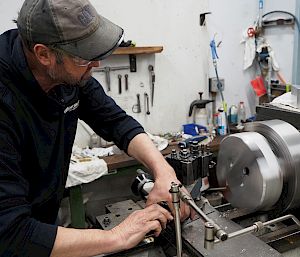 An expeditioner wearing a cap works on a turning machine.