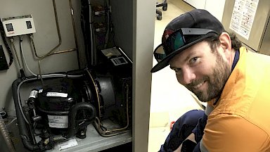 Man working on motor at back of fridge.
