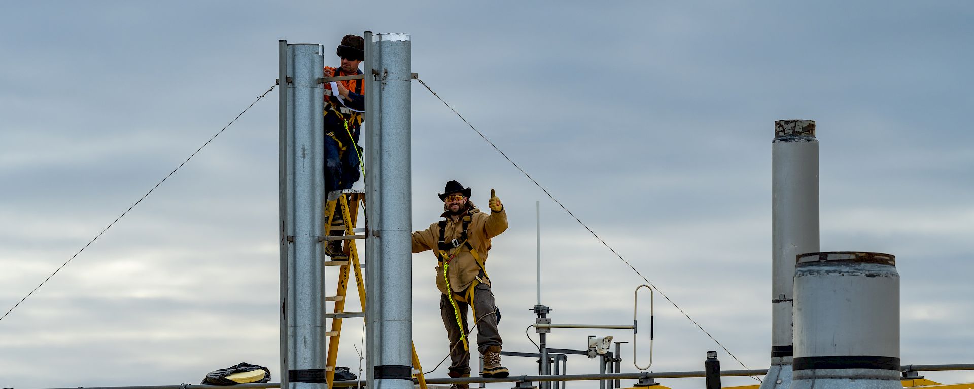 2 expeditioners work on the roof of a yellow building.