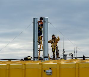 2 expeditioners work on the roof of a yellow building.