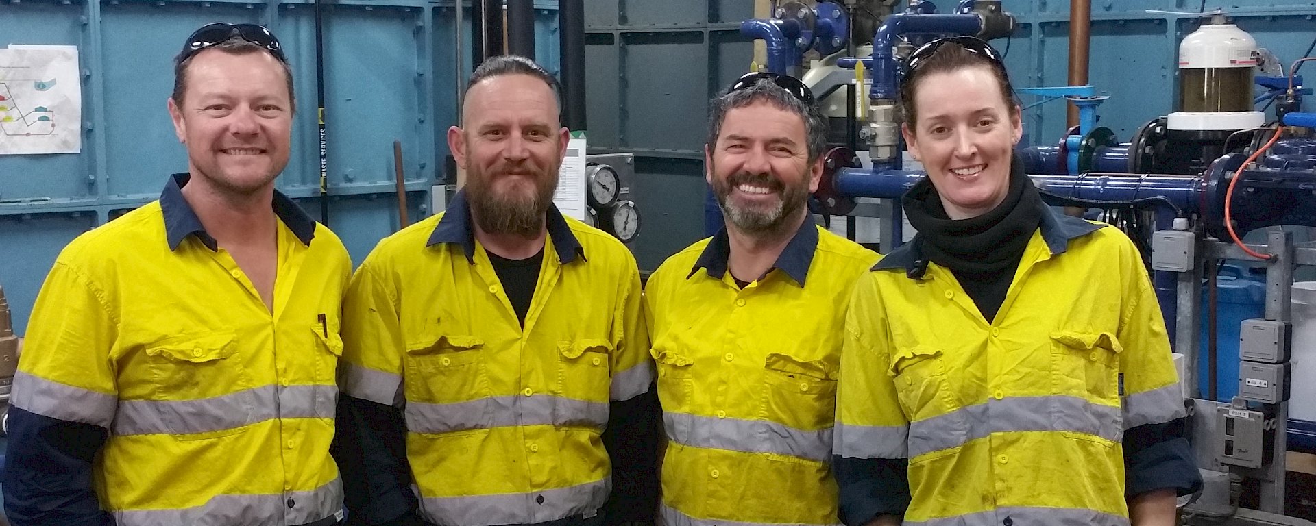 Four people in high visibility clothing in workshop, smiling at camera.