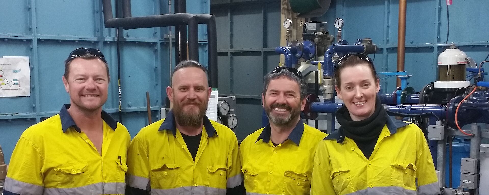 Four people in high visibility clothing in workshop, smiling at camera.