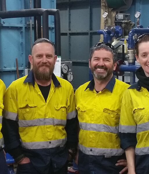 Four people in high visibility clothing in workshop, smiling at camera.