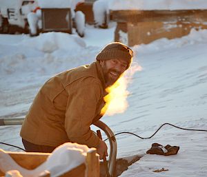 Bearded man using tools in snow.