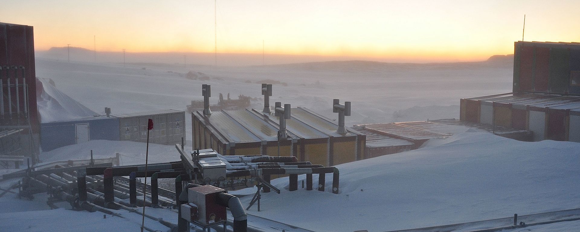 Aerial view of service piping leading from buildings with snowdrift, golden horizon in the background.
