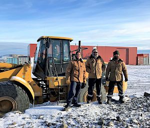 Three expeditioners stand in front of yellow tractor vehicle.