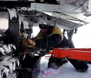 Mechanic making repairs underneath vehicle, kneeling in the ice.