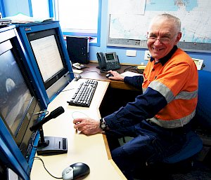 Man sitting at control desk with screens and phone.