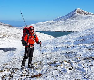 Person posing in snowy landscape with lake in background, antennae in backpack.