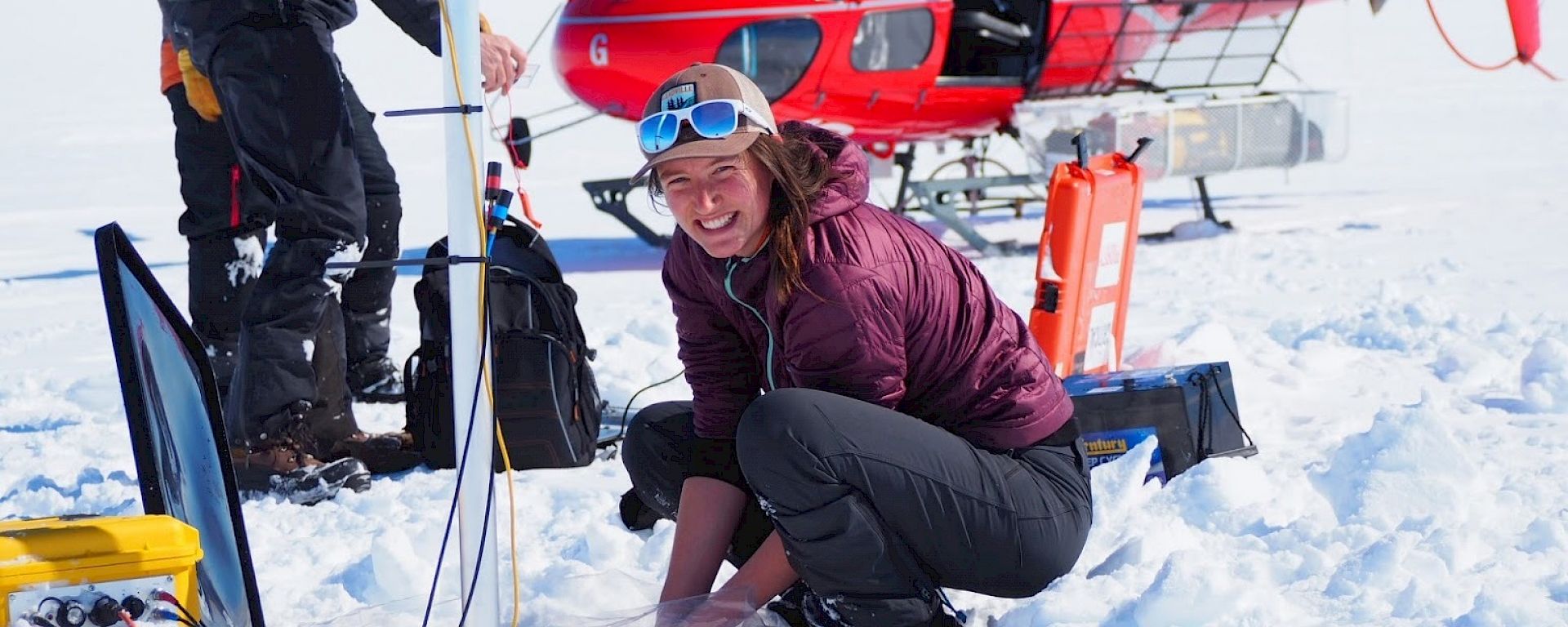 Scientists set up instruments in the ice in front of a red helicopter.