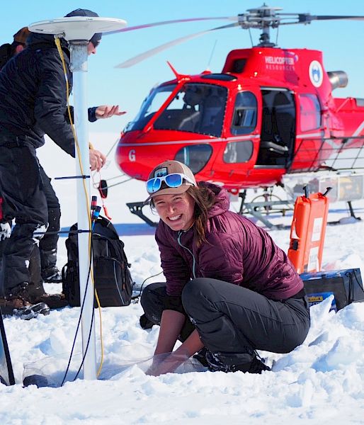 Scientists set up instruments in the ice in front of a red helicopter.