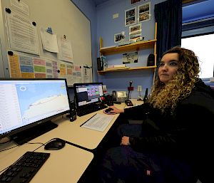 An expeditioner sits in front of a computer, which features a widescreen monitor showing a map.